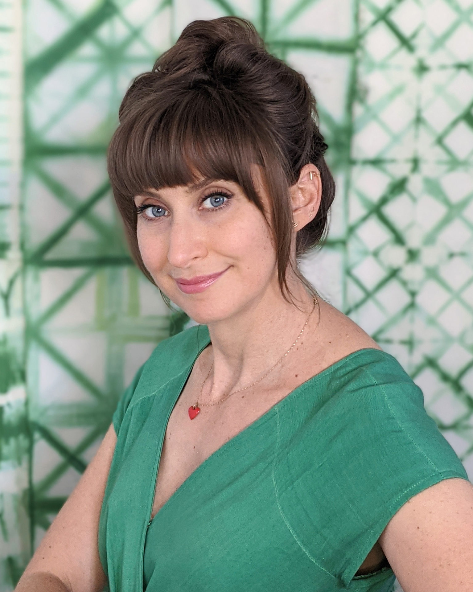 Portrait of a woman in a green dress set against an out of focus green and white patterned background.